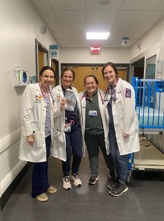 four residents wearing white coats and standing in a hospital corridor